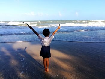 Rear view of woman standing at beach against sky