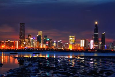 Illuminated buildings by river against sky at night