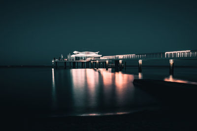 Illuminated pier by sea against clear sky at night