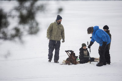 Mature men ice fishing with sons at frozen lake during vacation