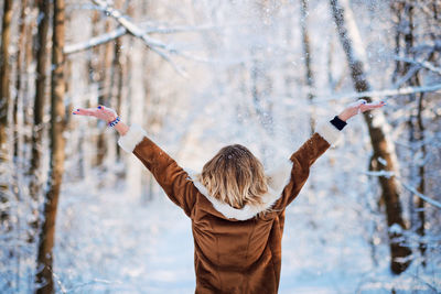 Rear view of happy woman throwing snow while standing in forest