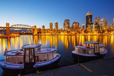 Ferry boats moored against illuminated burrard bridge in granville island