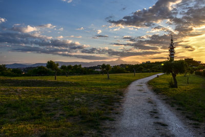 Road amidst field against sky during sunset