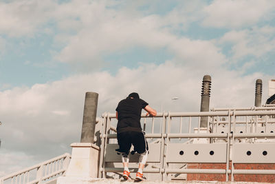 Rear view of man standing by railing against sky