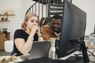 Male and female computer programmers looking at laptop in office