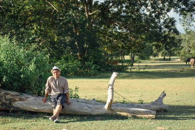 Portrait of man sitting on fallen tree at forest