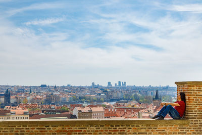 A man sits on a brick wall and admires the panorama of prague.