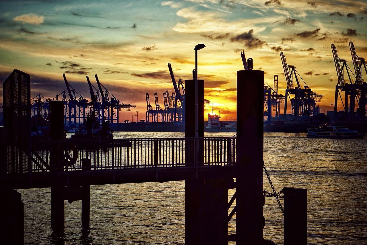 SILHOUETTE OF WOODEN POSTS IN HARBOR AGAINST SKY