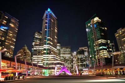 Illuminated modern buildings in city against sky at night