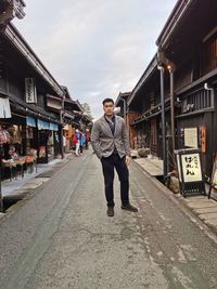 Full length portrait of young man standing on street against sky