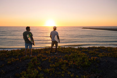 Rear view of man standing at beach against sky during sunset