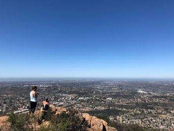 People looking at cityscape against clear blue sky