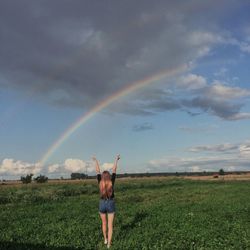 Rear view of teenage girl standing on field against rainbow