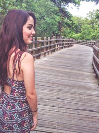 Beautiful smiling woman standing on wooden footbridge at forest