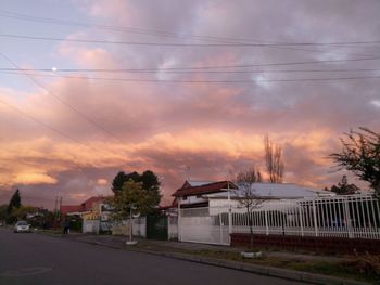 Road by buildings against sky during sunset