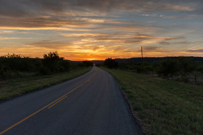 Road leading off into some orange and yellow clouds glowing in the sunset on the horizon.