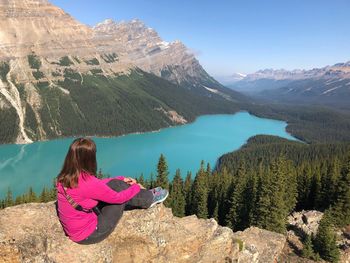 Rear view of woman sitting by lake against mountains