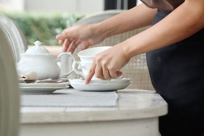 Midsection of woman picking crockery from table