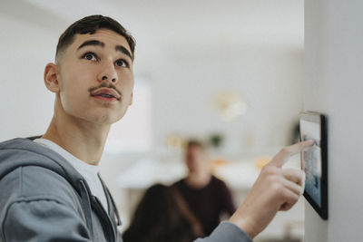 Teenage boy using home automation through digital tablet mounted on wall at home