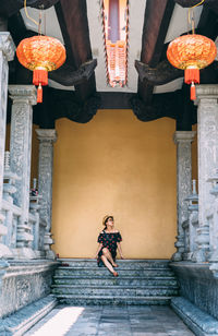 Full length of woman sitting at entrance of historic building