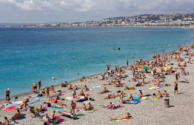 Crowded pebble beach in nice, france, in front of a turquoise blue sea