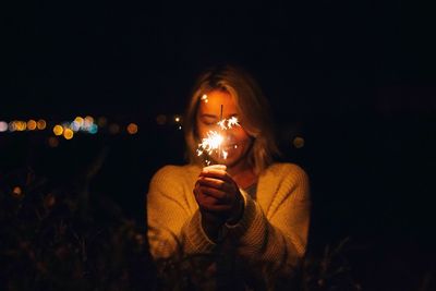 Close-up of woman holding illuminated light on field against sky at night