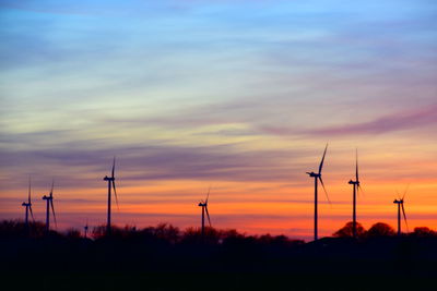 Silhouette of wind turbines on field against sky during sunset