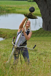 Cheerful young woman removing grass from brush cutter while standing at field