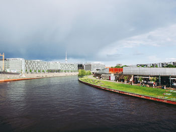 View of river by buildings against cloudy sky