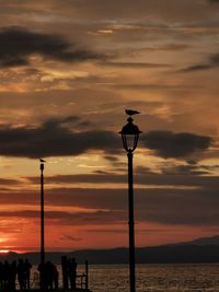 Street light by sea against sky during sunset