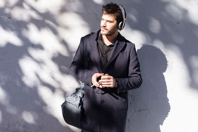 Smiling man looking away while standing by wall outdoors