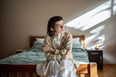 Pensive teen sitting on bed, looking at window, thinking of misunderstanding with friends, parents