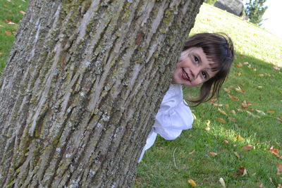 High angle portrait of cute girl hiding behind tree at park