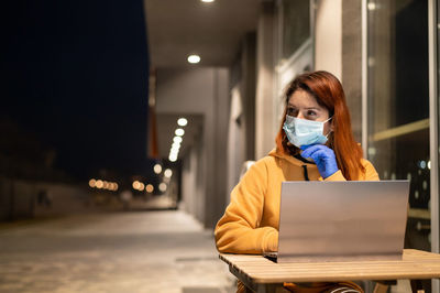 Businesswoman wearing mask using laptop in cafe at night