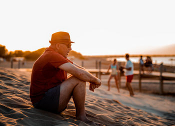 Man sitting on sand at beach against clear sky