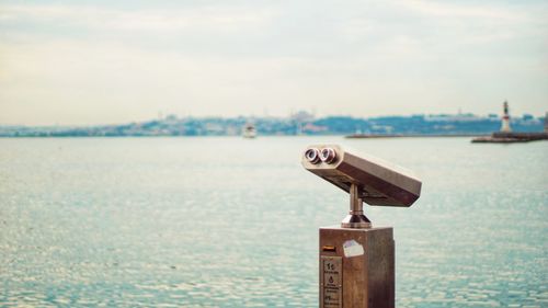 Close-up of coin-operated binoculars by sea against sky