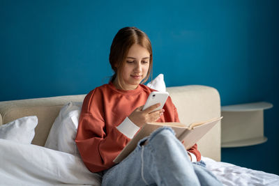 Portrait of young woman reading book while sitting on bed at home