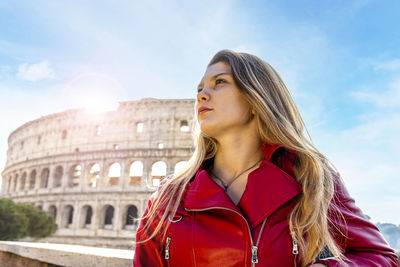 Backlight portrait of a young blonde woman posing in front of the colosseum.