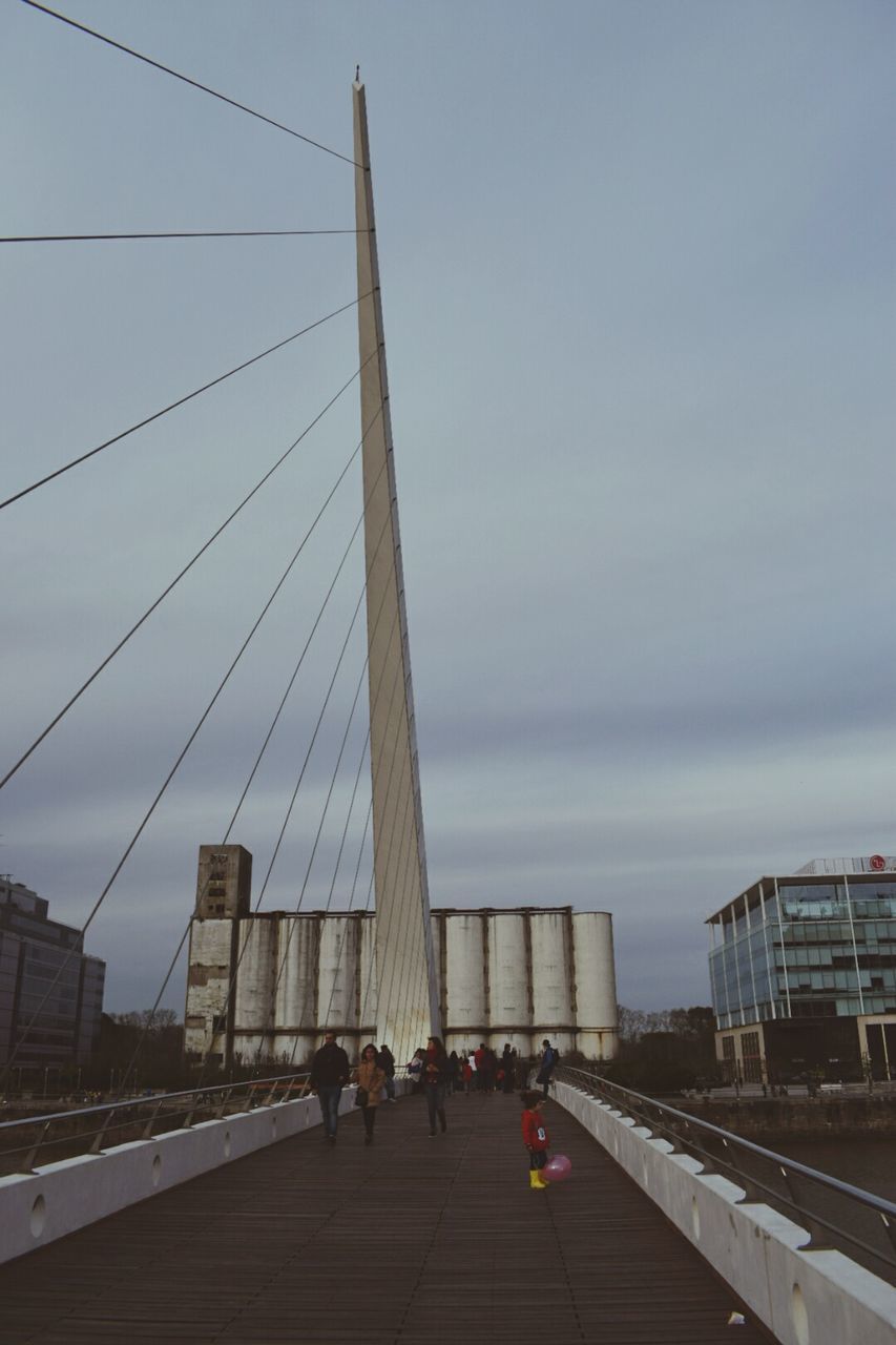 architecture, built structure, real people, men, connection, city, sky, transportation, lifestyles, bridge - man made structure, suspension bridge, women, outdoors, large group of people, building exterior, day, skyscraper, modern, people