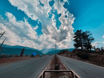 Empty road along plants and trees against sky