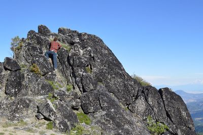 Rear view of man on rock against clear blue sky