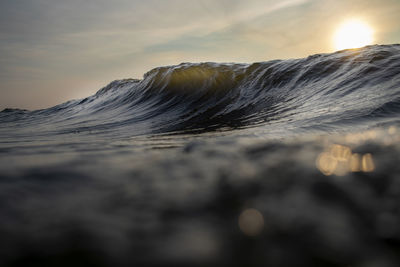 Close-up of wave on beach against sky during sunset