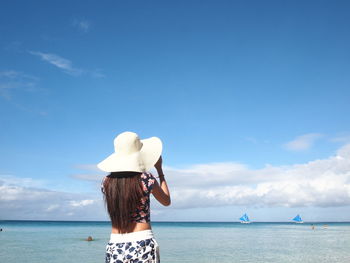 Rear view of woman standing on beach against blue sky