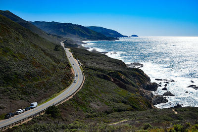 Scenic view of road by sea against clear blue sky