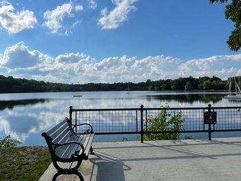 Bench by lake against sky