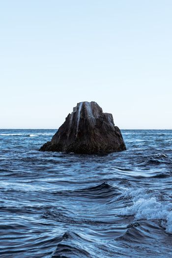 Rock formation in sea against clear sky
