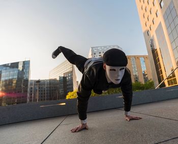 Man wearing mask doing handstand in city against clear sky