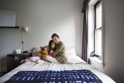 Mother embracing daughter while sitting on bed at home