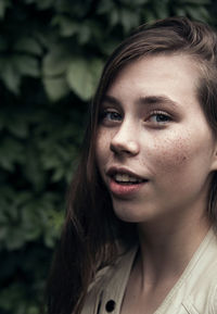 Close-up portrait of beautiful young woman by plant