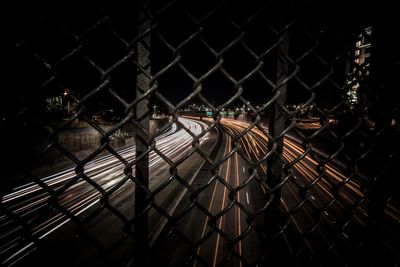 Light trails on road seen through chainlink fence